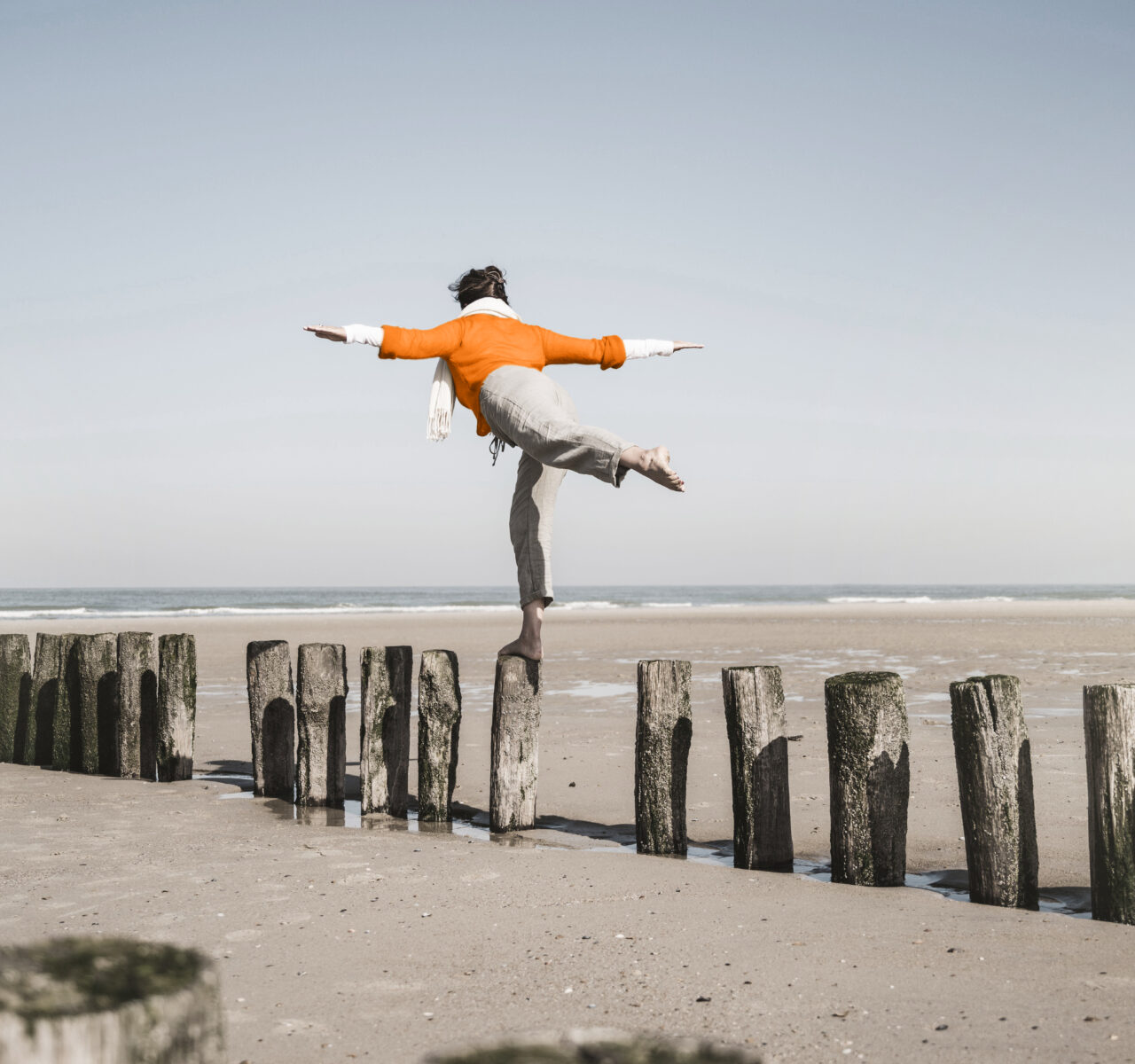 A person balancing on one leg atop a wooden post on a beach, symbolising the challenge of maintaining balance and stability during separation and divorce.