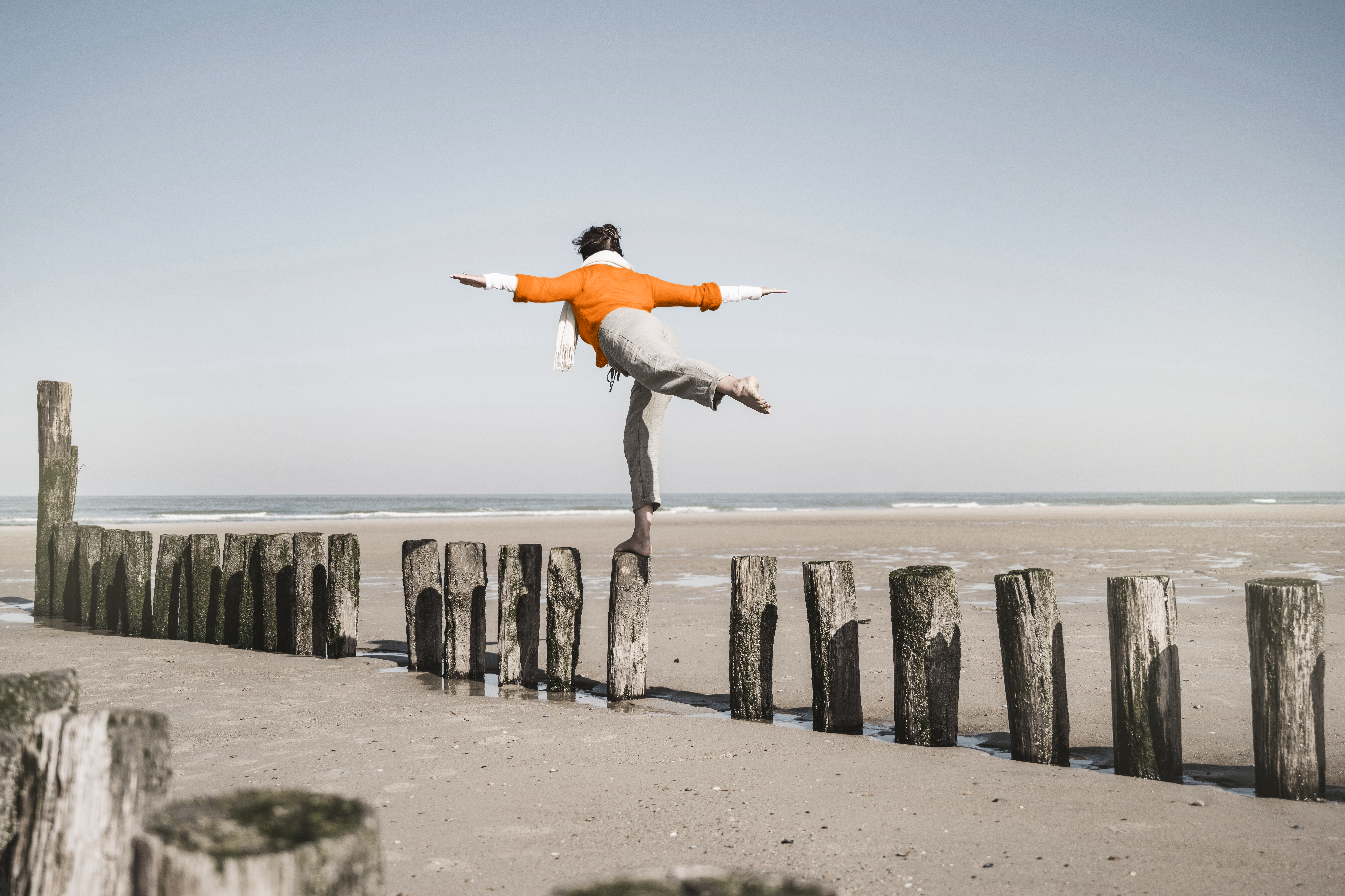 A person balancing on one leg atop a wooden post on a beach, symbolising the challenge of maintaining balance and stability during separation and divorce.