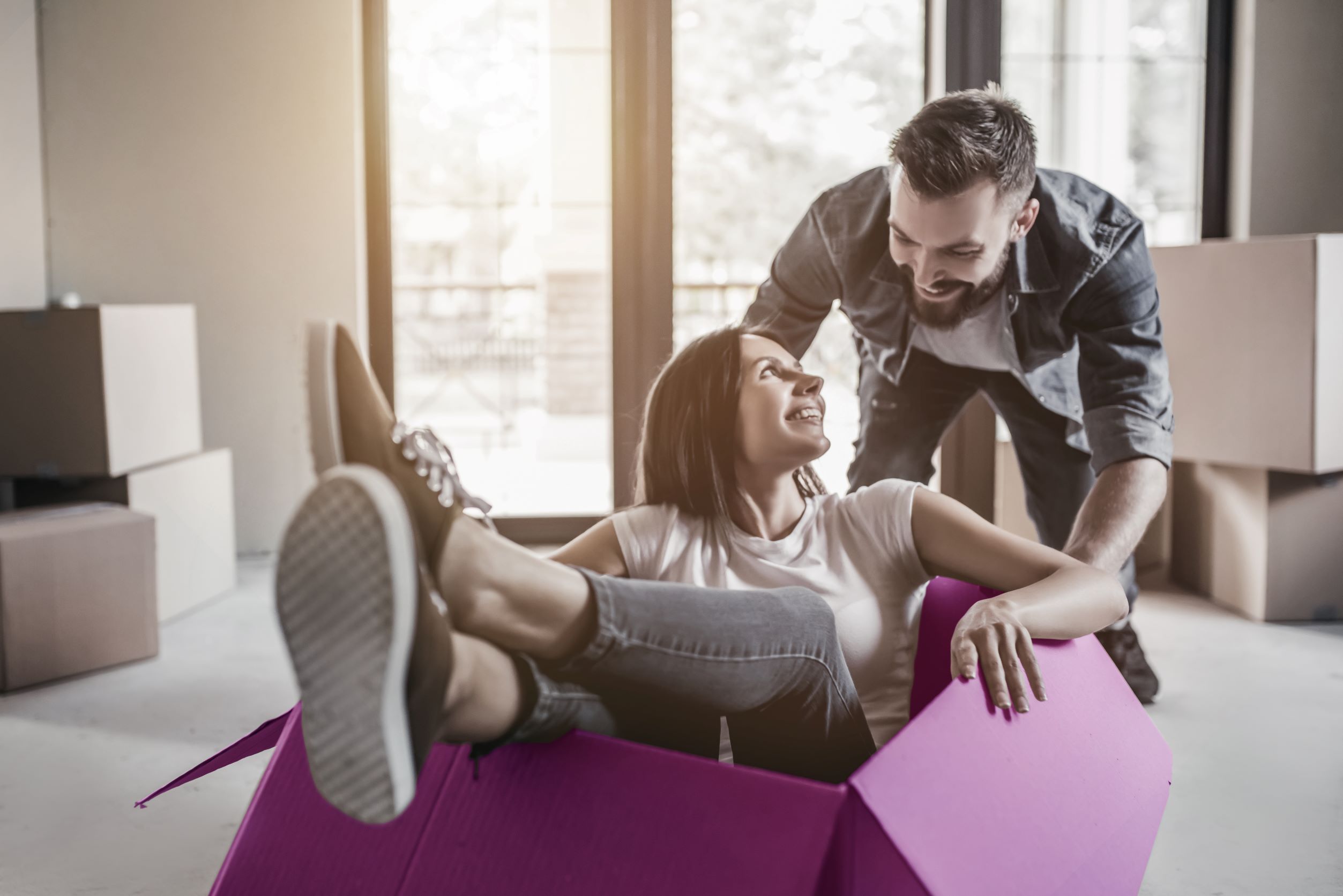 Two people enjoying a playful moment while moving into a new home, surrounded by cardboard boxes – representing the excitement and accessibility of shared ownership for first-time buyers.
